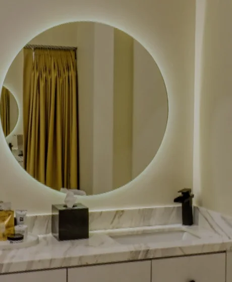 Lit round mirror over the marble vanity of a treatment room.