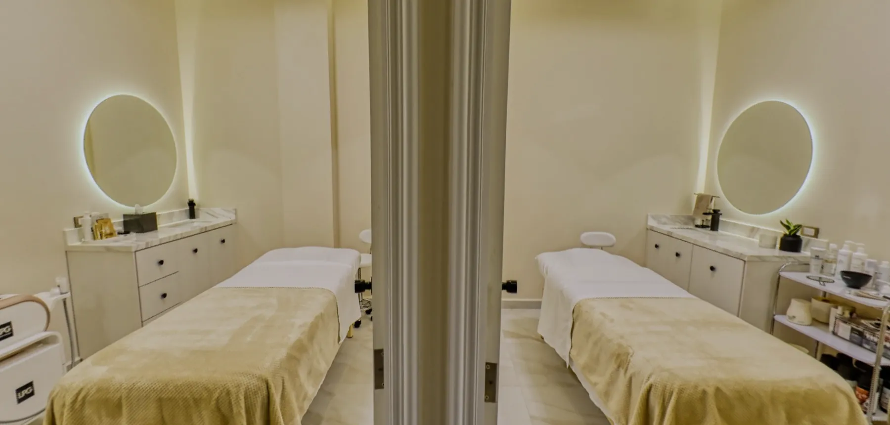 Two treatment rooms seen from the hallway, with their beds made up and their round mirrors lit.