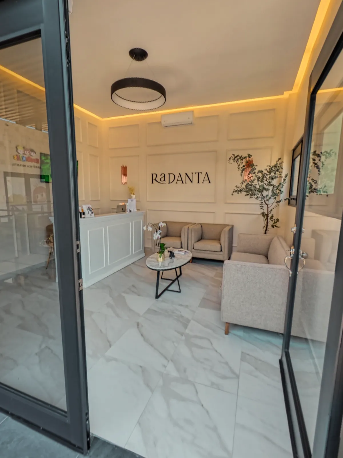 The glass door open from the plaza walkway, with the reception and the sign beyond.